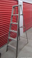 Aluminum step ladder shown in open position with five steps and side braces, photographed against red storage unit door.