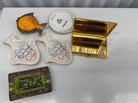 Top view of all six ashtrays along with the gold-tone cigarette holder case.