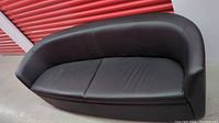 Front view of black leather curved couch inside a storage unit, showing two-seat cushion design and curved shape.