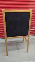Front view of the wooden framed blackboard side of the easel standing upright.