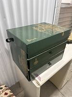 Front and side view of green Harrods box with three pull-out compartments and gold chandelier design on the side