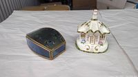 Two collectible items on a white cloth: Coalport fine bone china miniature house figurine and a vintage decorative box with bird motif.