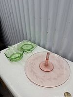 Pink glass center-handled sandwich tray with etched leaf design and two green depression glass serving dishes with double handles.