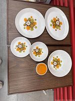 Top view of five pieces: two large plates, one medium plate, two small bowls and one small sugar jar, all with floral pattern on white ironstone.