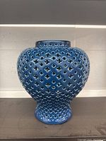 Front angle of large blue ceramic vase showing cutout pattern and bulbous body shape.