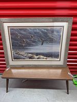 Framed artwork showing geese flying over water with a grey and blue cloudy sky background. Artwork signed by D.G. Brynaert, dimensions approximately 39x1x30 inches.