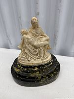 View of the Madonna della Pietà sculpture showing the Virgin Mary holding Jesus on a black oval base with gold accents.