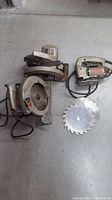 Three vintage power saws including two Skilsaw 7 1/4" circular saws and one Black & Decker jigsaw, shown with saw blades on floor.