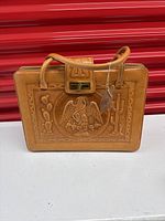 Full view of the tan leather purse showing embossed Mexican eagle and cactus motifs on the front with sturdy handles and clasp closure.