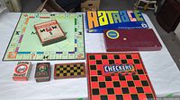 Overview of multiple vintage board games including Monopoly, Rat Race, Checkers, and various card games arranged on a white surface.
