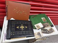 Photo capturing three scrapbooks on a white surface against a red backdrop, showing covers and some loose photos and postcards.