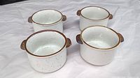 Photo showing four white speckled vintage stoneware pots with brown rims and dual small side handles grouped together