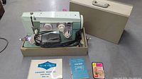 Vintage Viking sewing machine with case, owner's manual, quick steps guide, and light bulb all displayed together on floor.