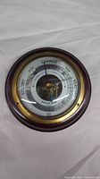 Front view of vintage barometer showing wood casing, brass bezel, glass cover, and dial with weather markings.