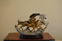 Full view of the sculpture showing three galloping horses on a dark oval base against a plain wall background.