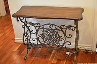Full view of the console table showing the wooden top and wrought iron base with scroll and floral patterns.