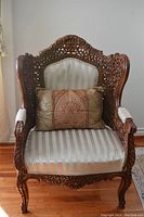 Full front view of the carved wood accent chair with beige striped fabric seat and decorative cushion