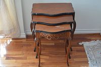 Top front view of three nested antique wooden tables showing the carved apron and curved legs