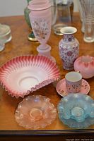 Photo showing the collection of antique ruffled edge bowls in rose-pink and sky-blue, three decorative vases in rose-pink, a rose-pink porcelain teacup with delicate gold floral painting, and plates and bowls with ruffled rims.