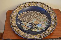 Large porcelain decorative bowl with navy blue background and detailed peacock and floral painting on a wooden table.