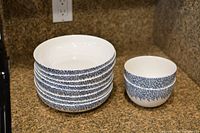 Stack of 8 shallow white porcelain dinner bowls with blue textured pattern on outside, next to 2 smaller deep bowls with same design.
