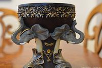 Close-up of the bowl showing the dark brown wood with gold painted detailing and sculpted blue resin elephants with gold accents and jewel decoration.