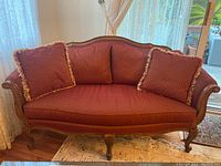 Front view of the burgundy loveseat sofa showing two large back pillows and two throw cushions. Upholstery has a gold dot pattern. Sofa frame has detailed carved wood legs and top rail.