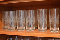 Eleven clear crystal highball glasses with detailed cut pattern, placed on a shelf.