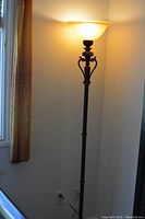 Full view of the tall floor lamp illuminated, showing the yellow/gold frosted glass shade and dark antique finish metal pole and base.