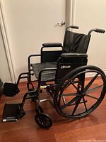 Side view of the black folding wheelchair showing steel frame, armrests, large rear wheels, footrests, and upholstery