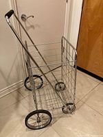 Image of lightweight metal grocery shopping cart, showing basket on four wheels with black rubber handle grip.
