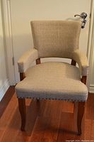 Side angled view of the accent chair showing the fabric upholstery, wooden legs, and nail head trim detail.