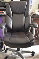 Front view of black leather ergonomic office chair with high back, cushioned lumbar support, padded armrests, silver base with wheels.