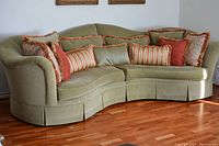 Side view of the curved green velvet sectional sofa showing the seat and leg area and throw pillows.