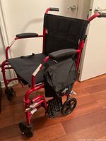 Right side angle of the red Medline transport wheelchair, showing the padded armrests, side storage bag, and front and rear wheels.