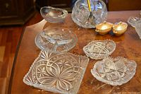 Six crystal bowls displayed on a wooden table including three Bohemian cut crystal bowls, visible clear crystal detailing, and small yellow porcelain jars with lids.