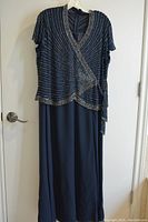 Full view of navy blue chiffon long formal dress hanging on hanger with light silver bead embellishments, V-neck, short sleeves and long skirt