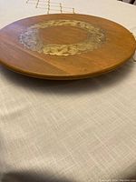 Top view of the wooden lazy Susan showing the round tray with an ornate gold floral/leaf border decoration around the center.