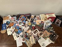 Wide top view of a large assortment of vintage travel-related printed materials including magazines, pins, patches, booklets, cards, and souvenirs spread out on a wooden floor.