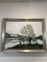 Full view of framed landscape painting showing a lakeside with trees and building reflection, signed by the artist.
