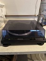 Front and top view of Onkyo CP-1055FII turntable with dust cover closed showing control buttons and base.