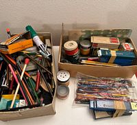 Two boxes filled with an assortment of vintage artist supplies including pens, pencils, ink bottles, paint jars, and packs of lead and nibs