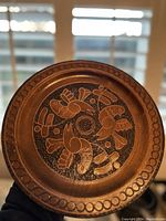 Front view of round wooden plate showing hand carved design of four birds with detailed patterns and decorative circular border.