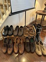 Front view of nine pairs of shoes arranged on a wooden two-tier shoe organizer rack near stairs and lamp.