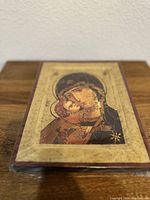 Angled photo showing the wooden plaque with the Holy Virgin Mary icon view, highlighting the gold leaf background and aging crackle texture