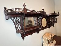 Angled front view of complete shelving unit mounted on wall showing central mirror, lattice sides and finials.