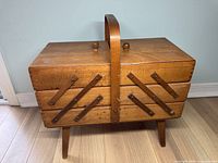 Closed accordion style wooden sewing box with handle and legs