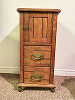 Front view of antique wooden smoker cabinet showing door and two drawers with original brass pulls.
