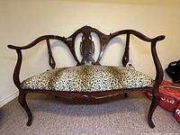 Front view of Art Nouveau wooden settee with leopard print cushion seat.