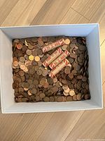 Top-down view of white cardboard box filled with loose pennies and six paper-wrapped penny rolls